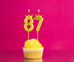 Birthday celebration with number 87 candle - Yellow cupcake on a pink background