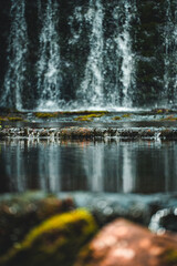Small natural waterfall flowing over a mossy rock wall in a forest. Tranquil nature scene with lush greenery and clean water.
