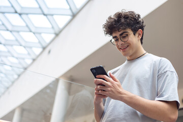 Smiling teenage boy using smartphone in modern urban space. Concept of youth lifestyle, digital...
