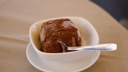 Spoon digging into a chocolate tartufo dessert covered with cocoa powder, served in a white bowl on a table in Pizzo, Italy