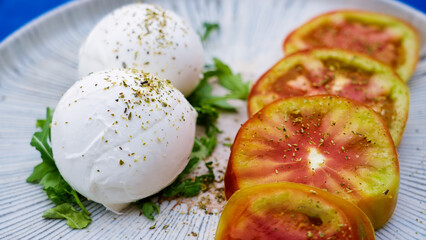 Two fresh Buffallo mozzarella balls seasoned with oregano, served with sliced tomatoes on a plate, representing italian cuisine