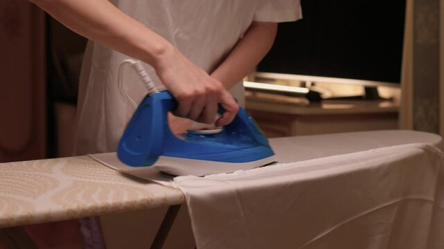 A person meticulously ironing clothes at home, ensuring all garments are neat and well cared for