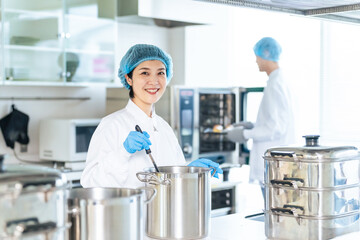 厨房で大鍋で調理する衛生白衣を着た女性調理師　給食センター　給食室