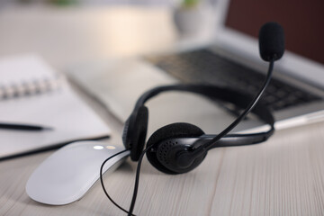 Headset with microphone and laptop on white wooden desk in office, closeup