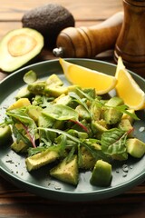 Tasty cut avocados with arugula, lemon and dressing on wooden table, closeup
