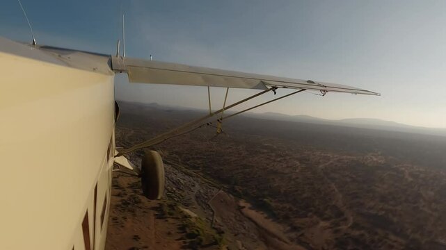Aerial wide of small air plane side view flying over dry savannah with shrubs, river and road in a sunny morning in Kenya