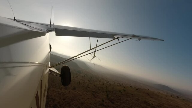 Aerial wide of small air plane side view flying over dry savannah with shrubs and hills in a sunny morning in Kenya