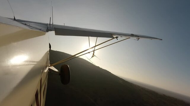 Aerial wide of small air plane side view flying over river and dry savannah hills in a sunny morning in Kenya