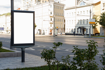 Vertical billboard near the road in the city. Sun illuminates the buildings very brightly. Mock-up.