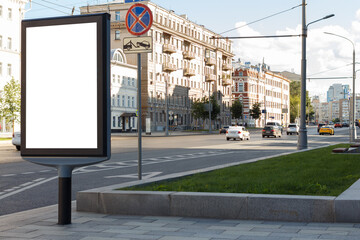 Vertical billboard near the road in the city, green lawn. Cars are driving. Mock-up.