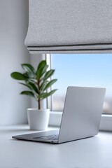 Fototapeta premium Modern minimalist workspace featuring a laptop and indoor plant by the window during daylight. UV Safety Month, National Stay Out of the Sun Day
