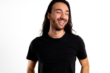 Young Latin man looks away and makes a big smile with braces on white background