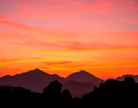 Orange pink sunset sky with mountain silhouette and dramatic clouds