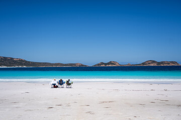 Three people relaxing on beach chairs facing turquoise ocean view