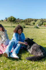 Mother and daughter petting their dog while having a picnic in a park