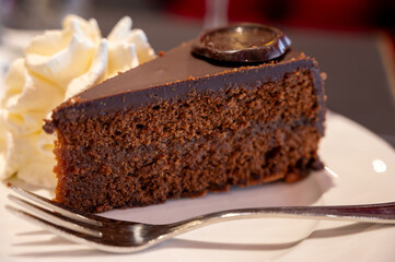 Piece of famous Sachertorte chocolate cake with apricot jam of Austrian origin served with whipped cream in old classic cafe-restaurant in Vienna