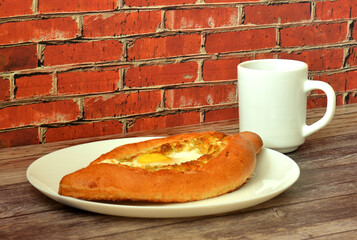 Khachapuri, traditional Georgian pie with cheese and egg on a wooden table, a cup of tea nearby.