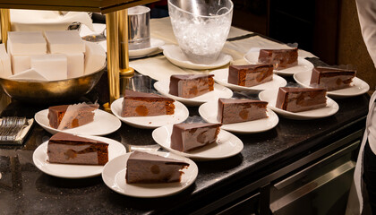 Many white plates with pieces of famous Sachertorte chocolate cake with apricot jam of Austrian origin in kitchen of old classic cafe-restaurant in Vienna