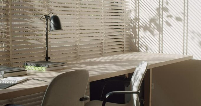 Bright, airy home office space bathed in sunlight. Wooden desk, simple decor, and blinds create a calm atmosphere. Perfect for productive work or creative inspiration.