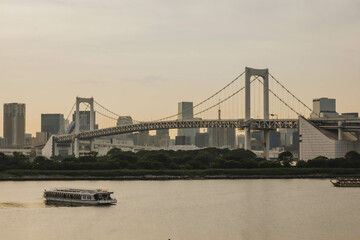 Cityscape of Tokyo skyline with the Rainbow Bridge and boat floating at Tokyo Bay in Odaiba area outdoor at sunset during spring in May in Tokyo city in Japan with space for text.