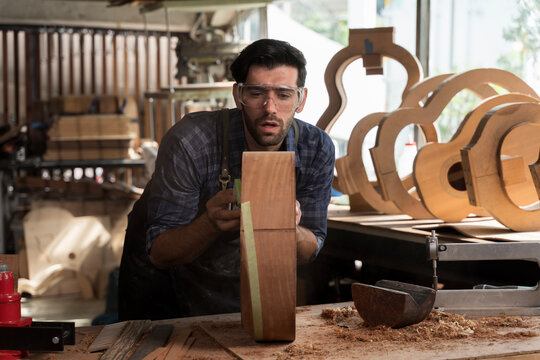 Focused carpenter working on wood shaping project in workshop, using tools for handmade custom guitar making