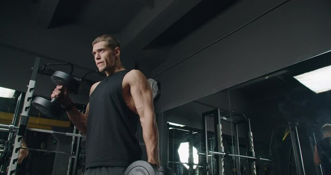 Young Athletic Man Lifting Weights in a Modern Gym. Focused young adult male lifting dumbbells in a well-equipped gym, displaying strength and determination.