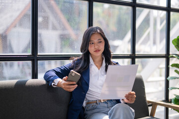 A woman is sitting on a couch with a cell phone in her hand