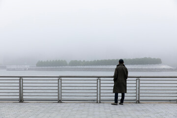Person on the waterfront looking at a foggy cityscape