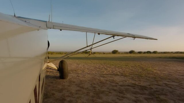 Wide of small air plane side view starting engine next to runway in savannah in a sunny morning in Kenya