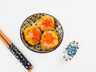 sushi Yellow dimsum or Siomay chicken and shrimp yellow dimsum chickwn and shrimp variance with carrot above served on white plate,chopsticks, wooden cutting board, in white background
