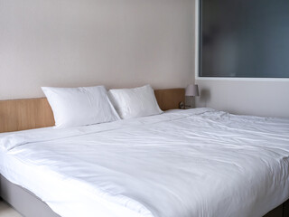 White clean bedroom in guest hotel room interior, white blanket with two pillows on simple wooden...