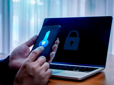 Two factor authentication or 2FA concept. Safety shield digital key icon on smart mobile phone screen in man hands while using laptop computer with padlock on display, cyber security technology.