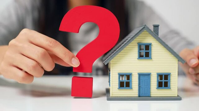 Red Question Mark Beside a Miniature Yellow House on a White Table Symbolizes Real Estate Uncertainty and Financial Investment Dilemmas