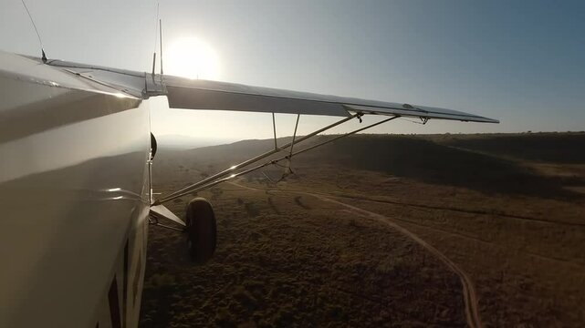 Aerial wide of small air plane side view flying over dry savannah with shrubs, road and hills in a sunny morning in Kenya