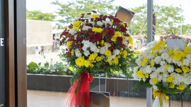 Flower stands with red, yellow, and white blooms arranged beautifully near a glass door, symbolizing congratulations or grand opening in a modern outdoor environment.
