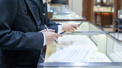 Businessmen in formal suits calculating and recording data with a calculator and pen on a jewelry...
