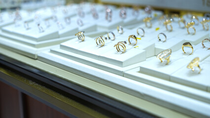 Assorted luxury rings in gold and silver on white display stands inside a jewelry store, showcasing...