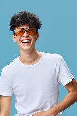 young man laughing wearing orange sunglasses and white t-shirt against blue background, joyful...