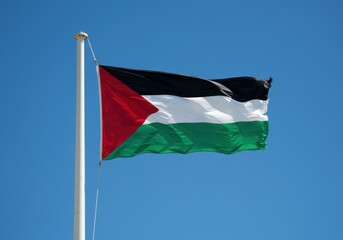 Palestinian flag waving in the wind against a clear blue sky