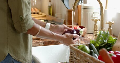Washing fresh green apple in kitchen sink with vegetables in basket nearby, at home - Powered by Adobe