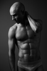 Fototapeta premium Black and white image of a muscular man striking a contemplative pose, showcasing strength and emotion. The simple background enhances the focus on his physique.