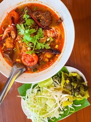 Traditional Thai noodle soup called “Nam Ngiao” served with fresh vegetables on the side. This Northern Thai dish features rice noodles in a spicy and tangy tomato-based broth with pork, dried chili