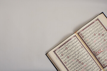 A close-up of open Quran pages with detailed Arabic calligraphy on a soft, neutral background.