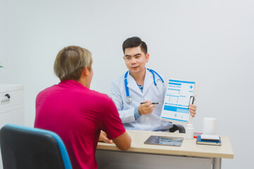 An experienced Asian male doctor consults with a male patient in a red shirt about men's health...