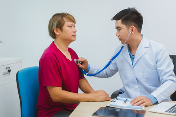An experienced Asian male doctor consults with a male patient in a red shirt about men's health concerns. He explains a medical form, providing expert advice on urology and related health conditions