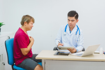 An experienced Asian male doctor consults with a male patient in a red shirt about men's health concerns. He explains a medical form, providing expert advice on urology and related health conditions