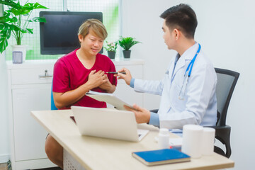 Fototapeta premium An experienced Asian male doctor consults with a male patient in a red shirt about men's health concerns. He explains a medical form, providing expert advice on urology and related health conditions