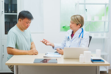 Asian male doctor specializing in cardiology explains heart disease to a patient using a heart...