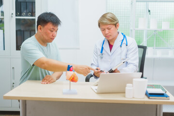 Asian male doctor specializing in cardiology explains heart disease to a patient using a heart...