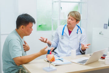 Asian male doctor specializing in cardiology explains heart disease to a patient using a heart...